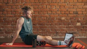 Athletic man sitting and resting on a mat in an urban gym, with a tablet and weights visible.